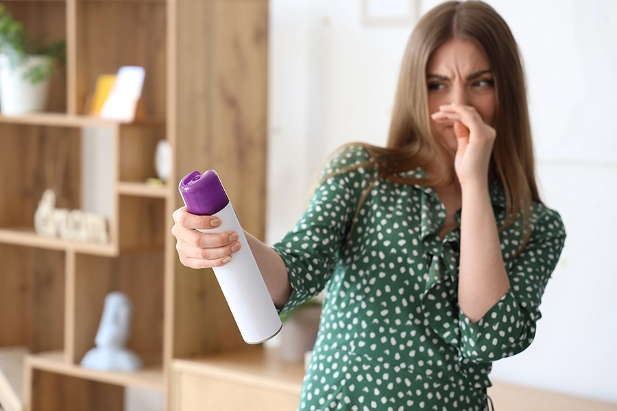 Woman in O'Fallon, IL home covering her nose from a bad smell with an air freshener can in her hand.