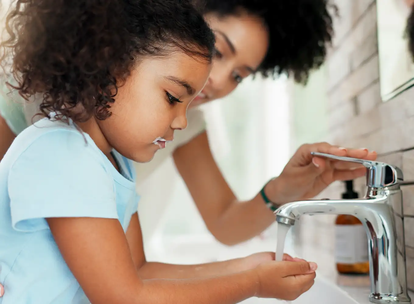 mom helping daughter at the bathroom sink