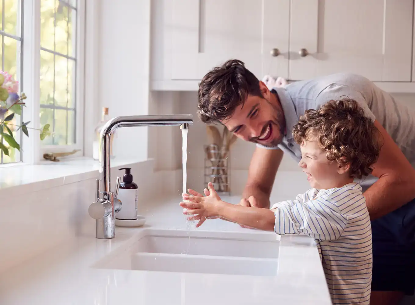 father and child washing hands in kitchen sink