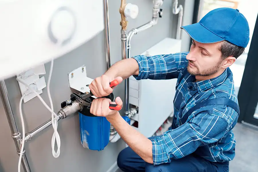 Polar—A young plumber in a blue uniform uses pliers while installing a water filtration system in a home in Belleville, IL.