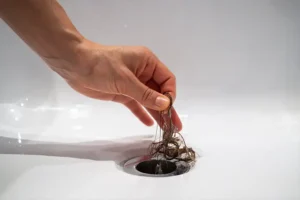 POLAR - Close-up image of a homeowner’s hand removing hair buildup from a clogged drain in a Belleville, IL home.